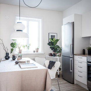 Idéer för att renovera ett litet minimalistiskt kök, med släta luckor, vita skåp, vitt stänkskydd, stänkskydd i porslinskakel, rostfria vitvaror, ljust trägolv och beiget golv