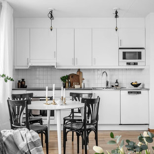 Exempel på ett skandinaviskt grå linjärt grått kök med öppen planlösning, med släta luckor, vita skåp, bänkskiva i rostfritt stål, vitt stänkskydd, beiget golv, vita vitvaror och ljust trägolv