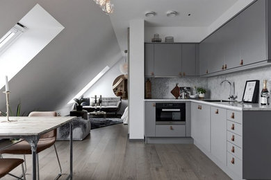 Пример оригинального дизайна: угловая кухня-гостиная в скандинавском стиле с плоскими фасадами, серыми фасадами и мраморной столешницей без острова