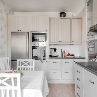 Skandinavisk inredning av ett grå grått kök, med luckor med profilerade fronter, beige skåp, vitt stänkskydd, rostfria vitvaror, ljust trägolv och beiget golv