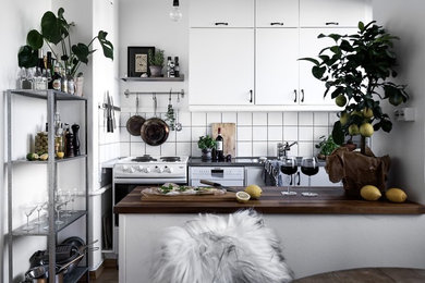 This is an example of a medium sized scandinavian single-wall kitchen in Stockholm with flat-panel cabinets, white cabinets, white splashback, white appliances, dark hardwood flooring, a breakfast bar, wood worktops and ceramic splashback.