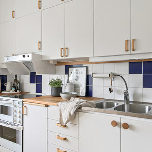 Inspiration för ett minimalistiskt linjärt kök, med en dubbel diskho, släta luckor, vita skåp, träbänkskiva, flerfärgad stänkskydd och vita vitvaror