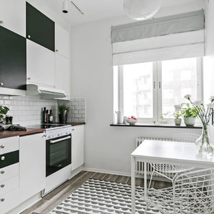 Bild på ett litet minimalistiskt linjärt kök och matrum, med släta luckor, vita vitvaror, brunt golv, vita skåp, vitt stänkskydd, stänkskydd i tunnelbanekakel och mörkt trägolv