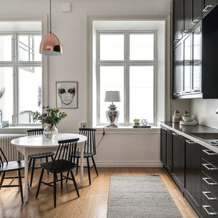 Idéer för skandinaviska linjära grått kök och matrum, med skåp i shakerstil, svarta skåp, vitt stänkskydd, stänkskydd i mosaik, rostfria vitvaror, ljust trägolv och beiget golv