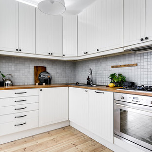 Inspiration för små skandinaviska beige kök, med vita skåp, träbänkskiva, grått stänkskydd, ljust trägolv, en nedsänkt diskho, rostfria vitvaror, beiget golv och luckor med profilerade fronter