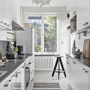 Foto på ett avskilt, litet nordiskt parallellkök, med släta luckor, vita skåp, granitbänkskiva, svart stänkskydd, vita vitvaror och grått golv