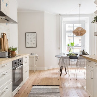 Bild på ett minimalistiskt kök, med en rustik diskho, luckor med upphöjd panel, vita skåp, vitt stänkskydd, stänkskydd i tunnelbanekakel, svarta vitvaror och ljust trägolv