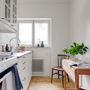 Nordisk inredning av ett avskilt beige linjärt beige kök, med en nedsänkt diskho, luckor med upphöjd panel, vita skåp, träbänkskiva, vitt stänkskydd, stänkskydd i tunnelbanekakel, vita vitvaror, ljust trägolv och beiget golv