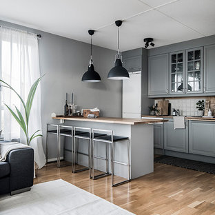 Foto på ett skandinaviskt brun kök, med luckor med upphöjd panel, grå skåp, träbänkskiva, vitt stänkskydd, stänkskydd i keramik, vita vitvaror, mellanmörkt trägolv, en halv köksö och beiget golv