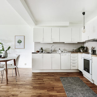 Idéer för ett nordiskt kök, med en integrerad diskho, släta luckor, vita skåp, bänkskiva i rostfritt stål, grått stänkskydd, vita vitvaror och mellanmörkt trägolv