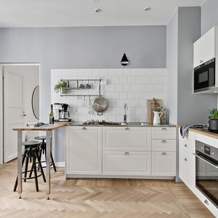 Idéer för att renovera ett avskilt nordiskt brun brunt l-kök, med en integrerad diskho, luckor med upphöjd panel, vita skåp, träbänkskiva, vitt stänkskydd, svarta vitvaror, ljust trägolv och beiget golv
