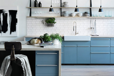 マルメにある広い北欧スタイルのおしゃれなキッチン (木材カウンター、エプロンフロントシンク、フラットパネル扉のキャビネット、青いキャビネット、白いキッチンパネル、セラミックタイルのキッチンパネル、パネルと同色の調理設備、淡色無垢フローリング、ベージュの床、ベージュのキッチンカウンター) の写真