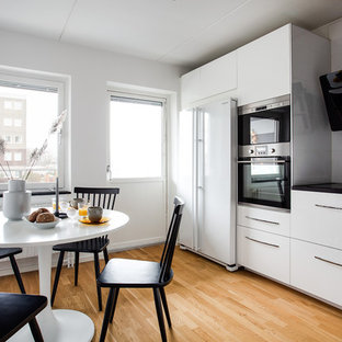 Idéer för minimalistiska svart kök och matrum, med släta luckor, vita skåp, grått stänkskydd, vita vitvaror och ljust trägolv