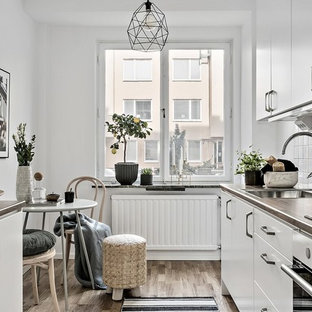 Idéer för skandinaviska brunt parallellkök, med en nedsänkt diskho, släta luckor, vita skåp, vitt stänkskydd, rostfria vitvaror och brunt golv