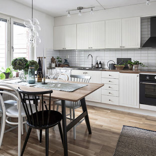 Skandinavisk inredning av ett mellanstort linjärt kök och matrum, med en dubbel diskho, vita skåp, träbänkskiva, vitt stänkskydd, svarta vitvaror, mellanmörkt trägolv och brunt golv