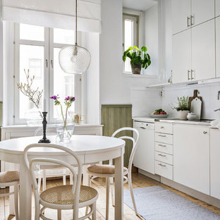 Bild på ett mellanstort minimalistiskt linjärt kök och matrum, med släta luckor, vita skåp, bänkskiva i rostfritt stål, vitt stänkskydd, beiget golv och ljust trägolv