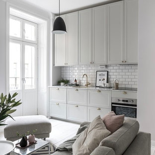 Exempel på ett minimalistiskt grå linjärt grått kök med öppen planlösning, med en undermonterad diskho, skåp i shakerstil, grå skåp, vitt stänkskydd, stänkskydd i tunnelbanekakel, integrerade vitvaror, ljust trägolv och beiget golv