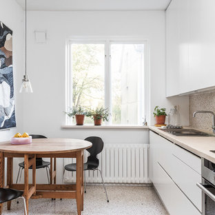 Foto på ett mellanstort skandinaviskt linjärt kök och matrum, med en dubbel diskho, vita skåp, träbänkskiva, rostfria vitvaror, terrazzogolv och släta luckor