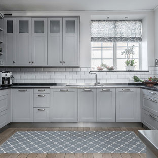 Inspiration för mellanstora minimalistiska svart u-kök, med en trippel diskho, skåp i shakerstil, grå skåp, vitt stänkskydd, stänkskydd i tunnelbanekakel, rostfria vitvaror och ljust trägolv