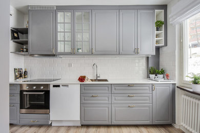 Exempel på ett stort nordiskt linjärt kök, med en enkel diskho, luckor med upphöjd panel, grå skåp, vitt stänkskydd, stänkskydd i keramik, rostfria vitvaror och ljust trägolv