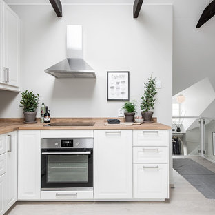 Foto på ett litet nordiskt kök, med vita skåp, träbänkskiva, grått golv, en nedsänkt diskho, luckor med upphöjd panel, rostfria vitvaror och ljust trägolv