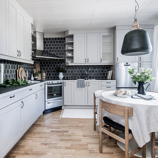 Bild på ett mellanstort minimalistiskt grå grått kök, med vita skåp, svart stänkskydd, ljust trägolv, beiget golv, en dubbel diskho, skåp i shakerstil, stänkskydd i tunnelbanekakel och rostfria vitvaror