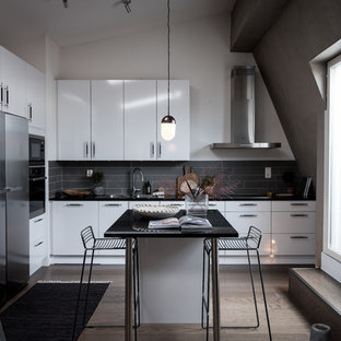Bild på ett minimalistiskt svart svart l-kök, med en dubbel diskho, släta luckor, vita skåp, grått stänkskydd, rostfria vitvaror, mellanmörkt trägolv, en köksö och brunt golv