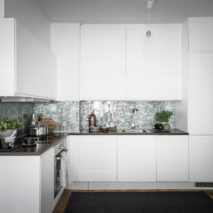 Inspiration för avskilda, mellanstora minimalistiska l-kök, med en enkel diskho, släta luckor, vita skåp, träbänkskiva, glaspanel som stänkskydd, integrerade vitvaror, mellanmörkt trägolv och blått stänkskydd