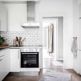 Idéer för ett skandinaviskt grå u-kök, med en integrerad diskho, släta luckor, vita skåp, bänkskiva i rostfritt stål, vitt stänkskydd, stänkskydd i keramik, vita vitvaror, mellanmörkt trägolv och brunt golv