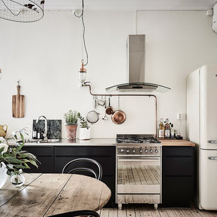 This is an example of a large industrial single-wall eat-in kitchen in Gothenburg with a double-bowl sink, flat-panel cabinets, black cabinets, stainless steel benchtops, stainless steel appliances, light hardwood floors and no island.