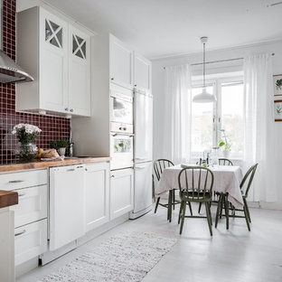 Idéer för ett skandinaviskt kök, med en nedsänkt diskho, luckor med infälld panel, vita skåp, träbänkskiva, rött stänkskydd, stänkskydd i mosaik, vita vitvaror, målat trägolv och vitt golv