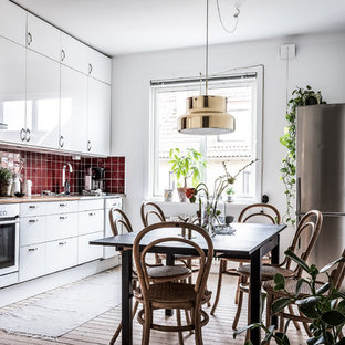 Nordisk inredning av ett linjärt kök och matrum, med släta luckor, vita skåp, träbänkskiva, rött stänkskydd, ljust trägolv, beiget golv, en nedsänkt diskho, stänkskydd i keramik och rostfria vitvaror