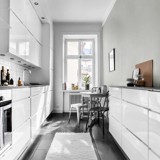 Idéer för ett minimalistiskt svart kök, med släta luckor, vita skåp, vitt stänkskydd, stänkskydd i tunnelbanekakel och svart golv