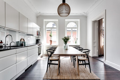 Skandinavisk inredning av ett mellanstort linjärt kök och matrum, med en enkel diskho, släta luckor, vita skåp, rostfria vitvaror, mörkt trägolv, vitt stänkskydd, glaspanel som stänkskydd och brunt golv