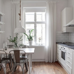 Idéer för att renovera ett minimalistiskt linjärt kök och matrum, med luckor med upphöjd panel, vita skåp, mellanmörkt trägolv, brunt golv, vitt stänkskydd, stänkskydd i tunnelbanekakel och vita vitvaror