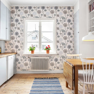 Inspiration for a mid-sized scandinavian single-wall eat-in kitchen in Stockholm with a drop-in sink, flat-panel cabinets, grey cabinets, wood benchtops, white splashback, stainless steel appliances, light hardwood floors and no island.