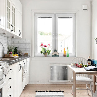Bild på ett minimalistiskt linjärt kök och matrum, med en enkel diskho, vita skåp, vitt stänkskydd, stänkskydd i tunnelbanekakel, ljust trägolv, släta luckor, vita vitvaror och beiget golv