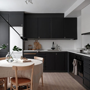 Foto på ett minimalistiskt kök, med en nedsänkt diskho, laminatbänkskiva, vitt stänkskydd, ljust trägolv, släta luckor, svarta skåp, svarta vitvaror och beiget golv