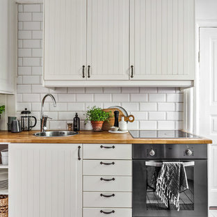 Inspiration för ett nordiskt beige linjärt beige kök, med vita skåp, träbänkskiva, vitt stänkskydd, rostfria vitvaror, en nedsänkt diskho, stänkskydd i tunnelbanekakel och släta luckor