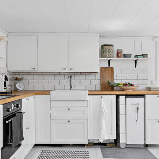 Idéer för ett mellanstort minimalistiskt beige l-kök, med en rustik diskho, luckor med infälld panel, vita skåp, träbänkskiva, vitt stänkskydd, stänkskydd i tunnelbanekakel, svarta vitvaror och grått golv