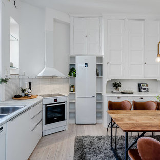 Inredning av ett minimalistiskt grå grått kök, med en dubbel diskho, luckor med infälld panel, vita skåp, vitt stänkskydd, vita vitvaror, ljust trägolv och beiget golv