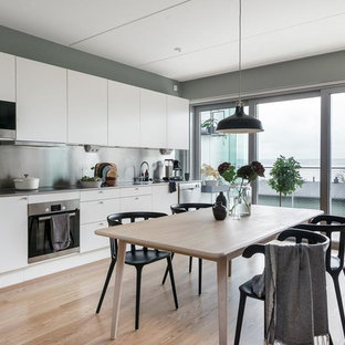 Idéer för att renovera ett minimalistiskt linjärt kök och matrum, med en integrerad diskho, släta luckor, vita skåp, bänkskiva i rostfritt stål, stänkskydd med metallisk yta, rostfria vitvaror och ljust trägolv