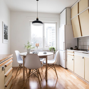 Idéer för att renovera ett mellanstort skandinaviskt parallellkök, med släta luckor, gula skåp, vita vitvaror, en integrerad diskho, bänkskiva i rostfritt stål, vitt stänkskydd och ljust trägolv