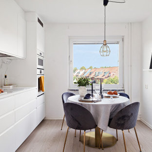 Foto på ett minimalistiskt vit linjärt kök och matrum, med släta luckor, vita skåp, vitt stänkskydd, stänkskydd i sten, vita vitvaror, ljust trägolv och beiget golv