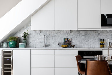 Inredning av ett minimalistiskt kök, med en undermonterad diskho, släta luckor, vita skåp, grått stänkskydd och rostfria vitvaror