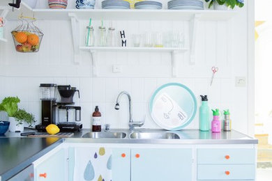 Kleine Skandinavische Küche ohne Insel in L-Form mit integriertem Waschbecken, flächenbündigen Schrankfronten, blauen Schränken, Edelstahl-Arbeitsplatte, Küchenrückwand in Weiß, Rückwand aus Keramikfliesen und Keramikboden in Sonstige