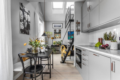 Inspiration för små minimalistiska linjära grått kök med öppen planlösning, med släta luckor, grå skåp, marmorbänkskiva, vitt stänkskydd, stänkskydd i porslinskakel, ljust trägolv och beiget golv