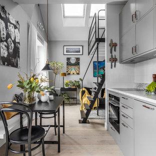 Inspiration för små minimalistiska linjära grått kök med öppen planlösning, med släta luckor, grå skåp, marmorbänkskiva, vitt stänkskydd, stänkskydd i porslinskakel, ljust trägolv och beiget golv