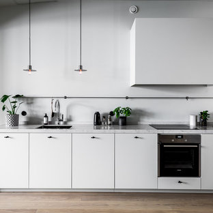 Minimalistisk inredning av ett mellanstort linjärt kök med öppen planlösning, med en enkel diskho, släta luckor, vita skåp, marmorbänkskiva, vitt stänkskydd, rostfria vitvaror, mellanmörkt trägolv och brunt golv