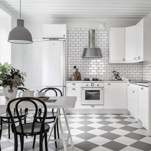 Inredning av ett minimalistiskt kök, med släta luckor, vita skåp, vitt stänkskydd, stänkskydd i tunnelbanekakel, vita vitvaror och flerfärgat golv